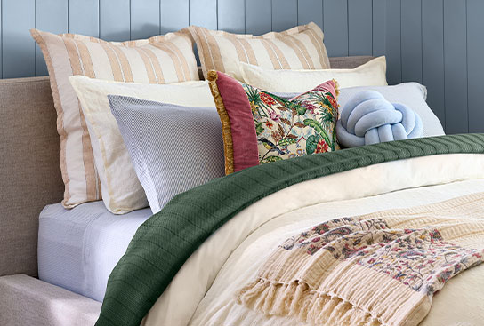 A beautifully made bed with decorative pillows, a fringe throw, a thick comforter & a sheet set.